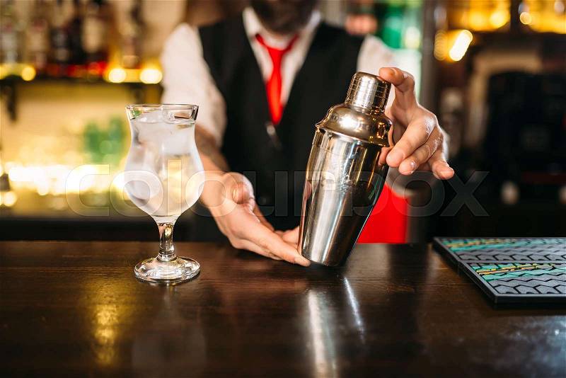 Barman with shaker behind a bar counter with glass of alcohol beverage, stock photo