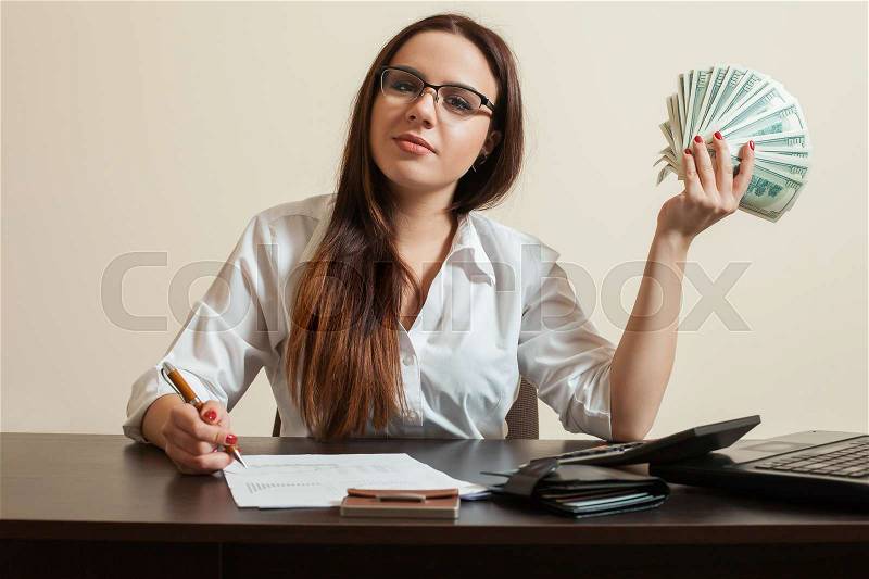 Female bookkeeper holding dollars fan in her hand. Business woman with money in hand signs financial documents, stock photo