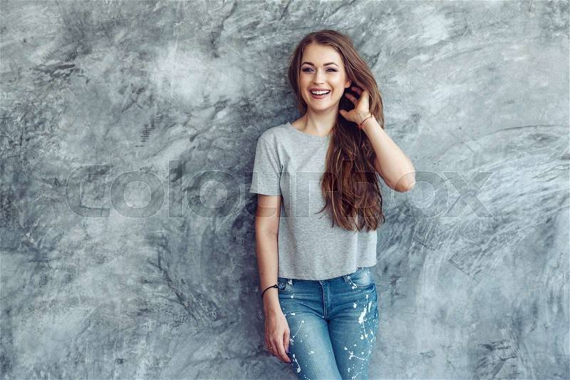 Young beautiful model wearing blank gray t-shirt and jeans posing against rough concgrete wall, minimalist street fashion style, stock photo