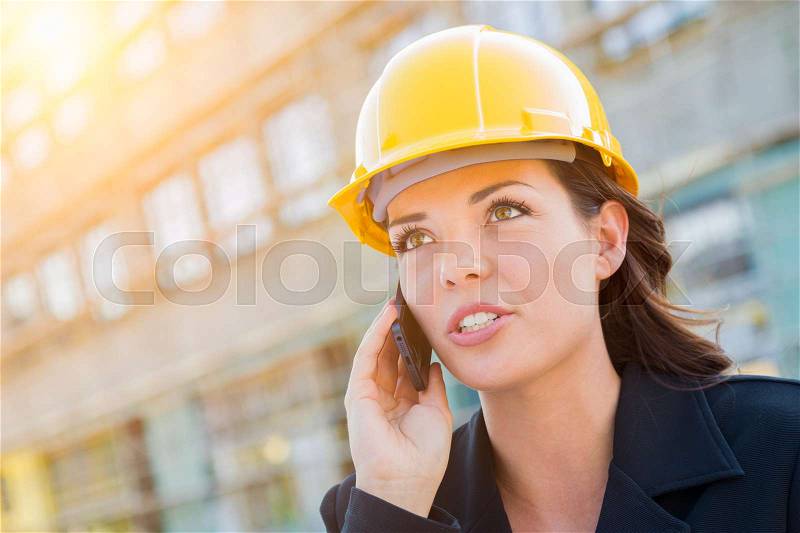 Young Professional Female Contractor Wearing Hard Hat at Contruction Site Using Cell Phone, stock photo