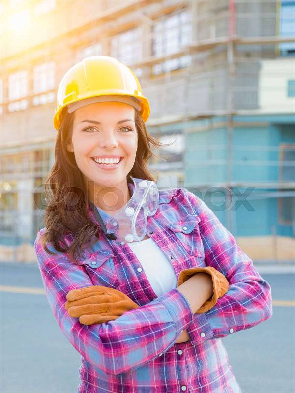 Portrait of Young Female Construction Worker Wearing Gloves, Hard Hat and Protective Goggles at Construction Site, stock photo
