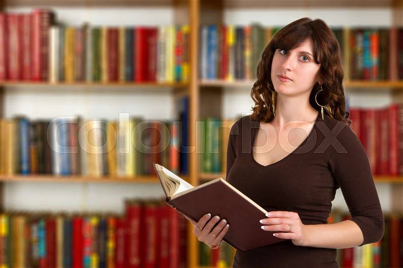 Portrait of clever student with book reading it in college library, stock photo