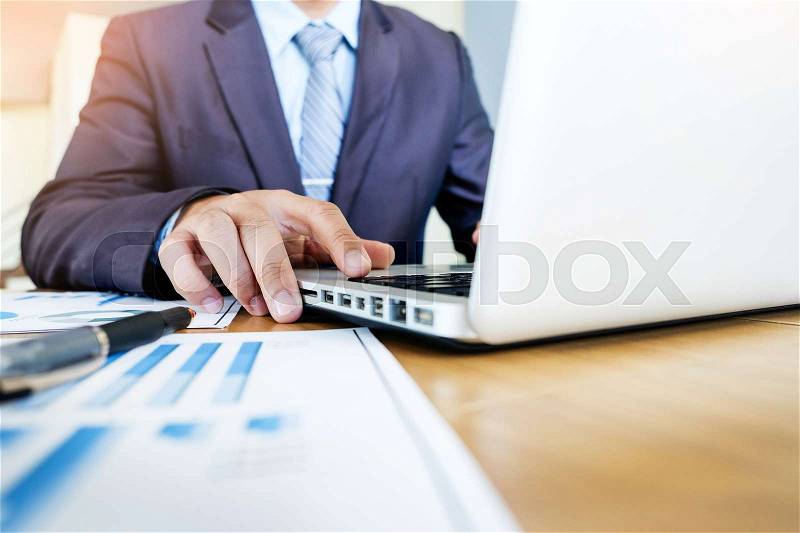 Working process startup. Businessman working with new finance project at office with laptop, tablet and graph data documents on his desk, stock photo