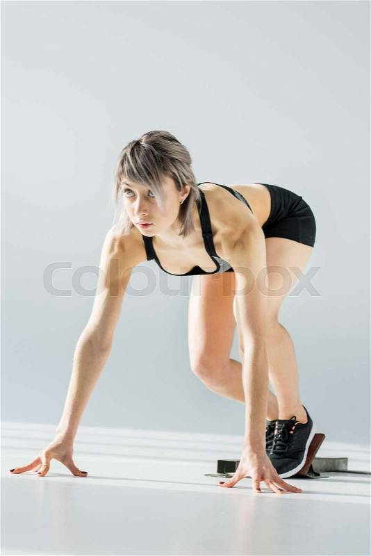 Attractive young sportswoman in starting position on grey, stock photo