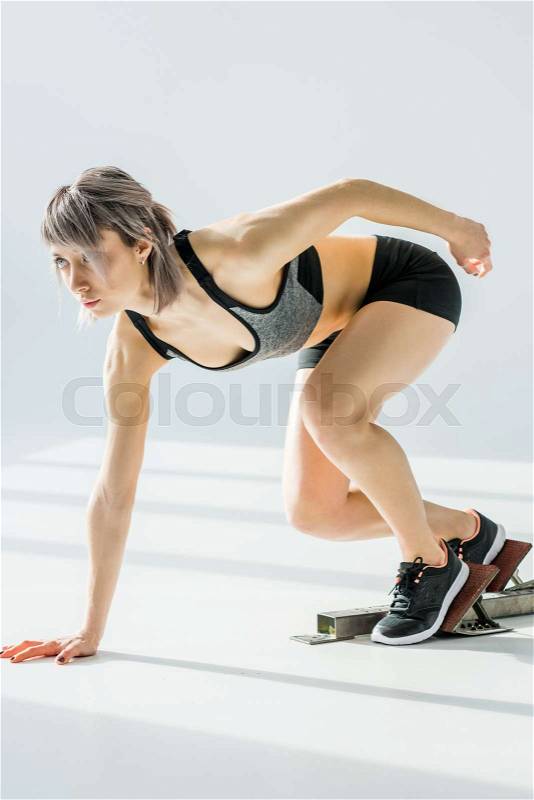 Side view of sporty woman in starting position on grey, stock photo
