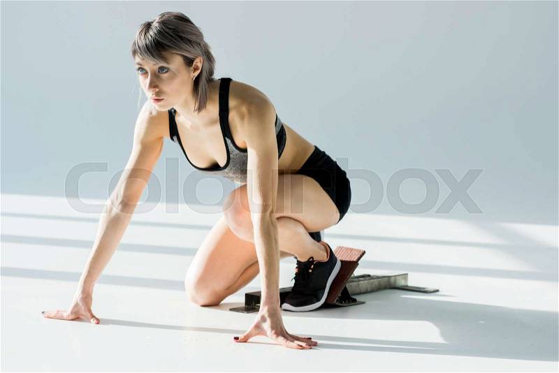 Side view of sporty woman in starting position on grey, stock photo