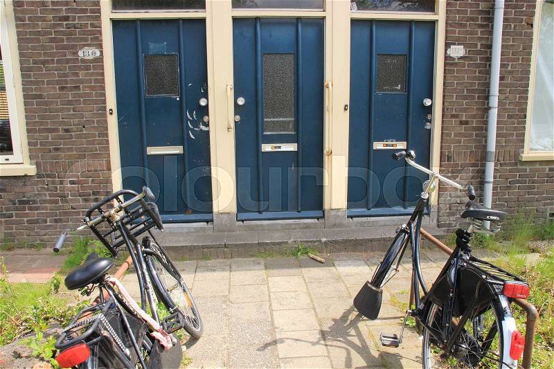 Parking place for bikes and three painted blue front doors of the terraced houses in the residential area in the city in spring, stock photo