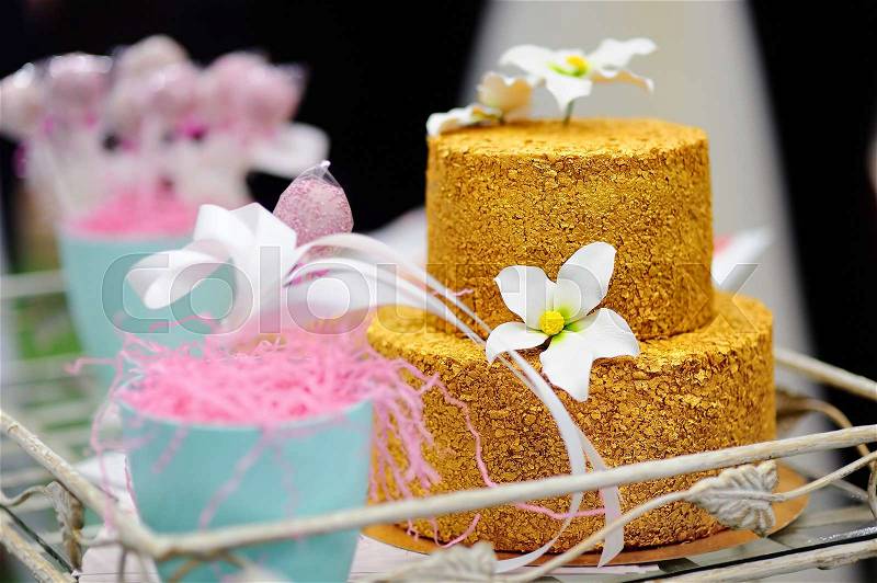 Gold wedding cake decorated with white sugar flowers. Sweet table on wedding party, stock photo