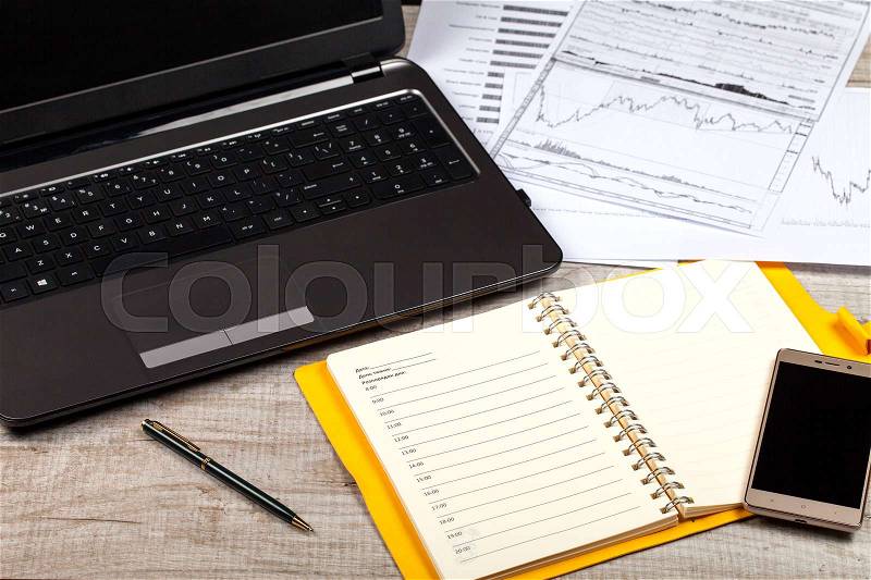 Open notebook, glasses, computer, pen and smartphone on a wooden table. Close-up, stock photo