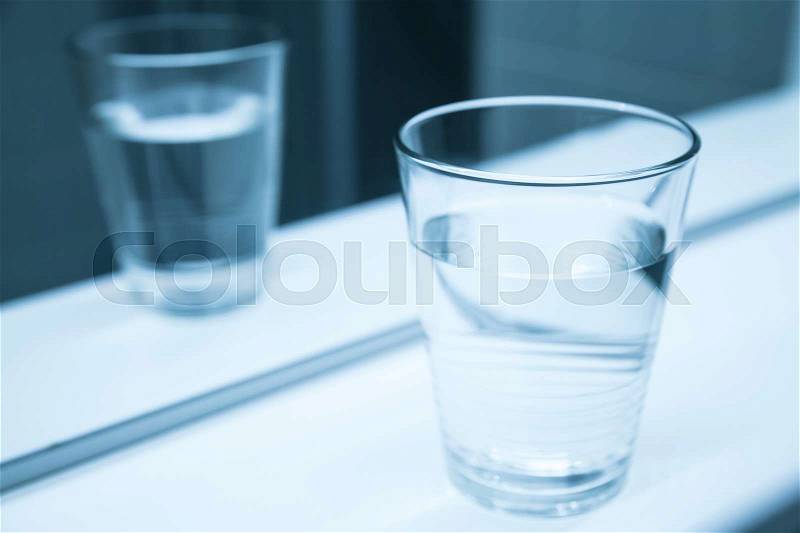 Glass of water stand on shelf near the mirror, blue toned close-up photo, stock photo