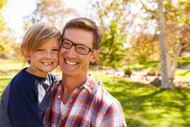 Father and seven year old son smiling to camera in a park, stock photo