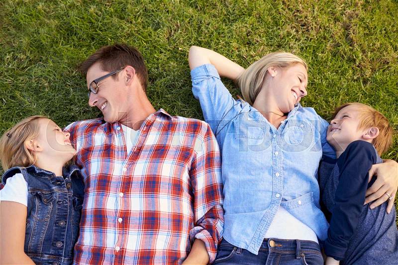 Young white family lying on grass in a park, waist up, stock photo