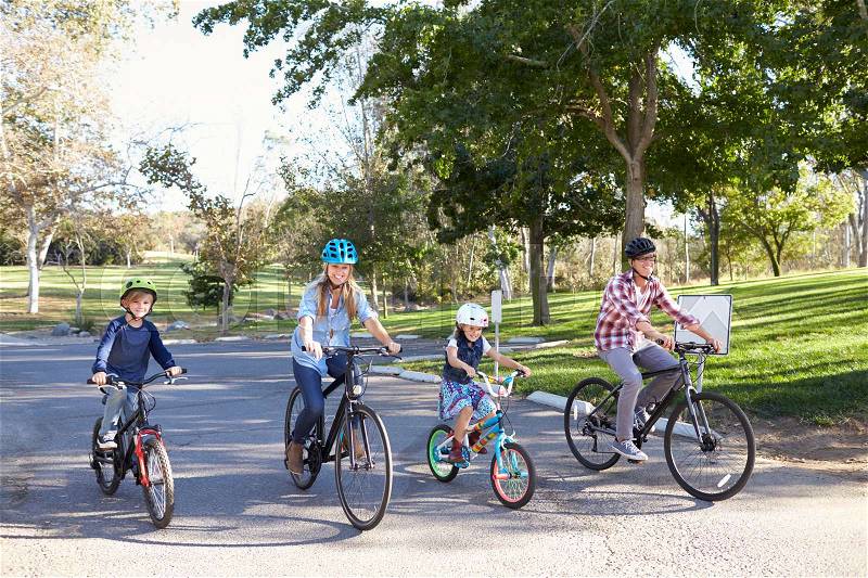 Young white family cycling together through a park, stock photo
