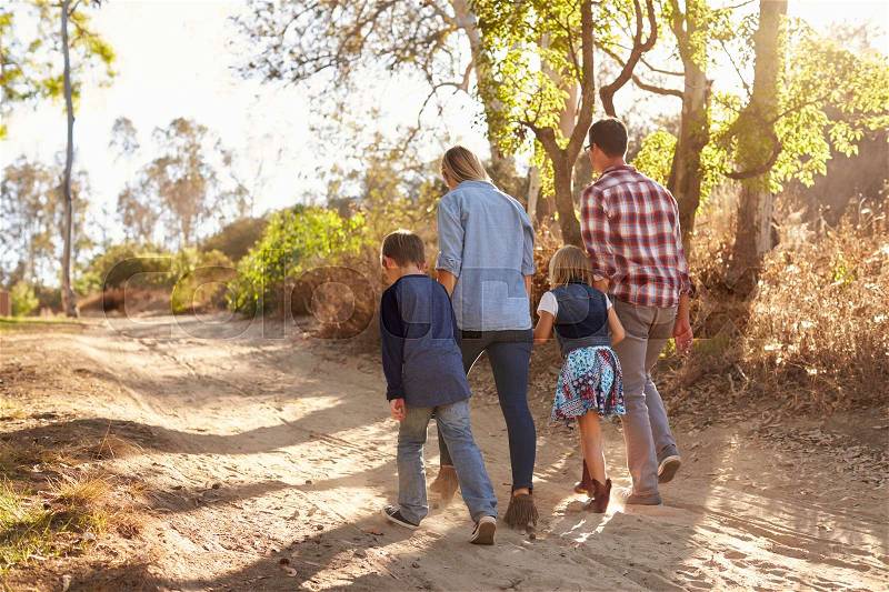 Young white family walking on a path in sunlight, back view, stock photo
