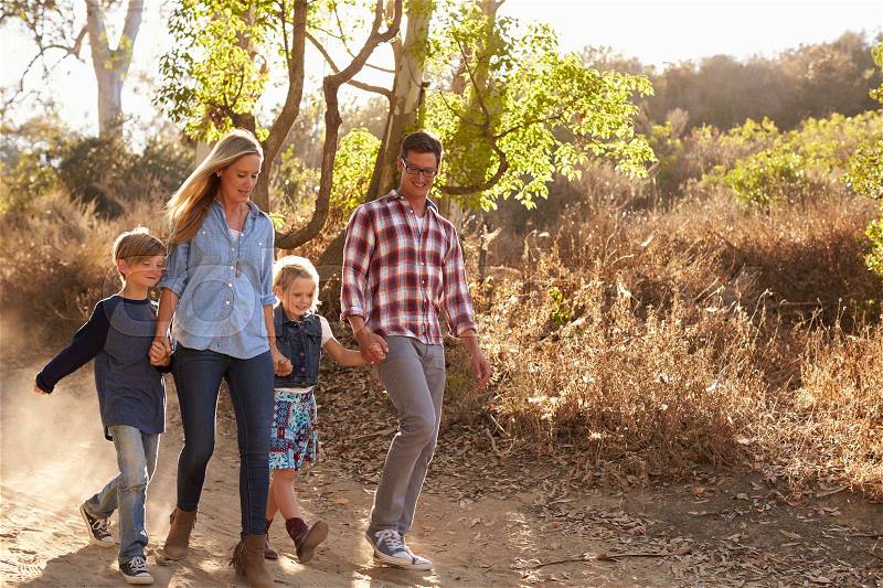 Young white family walking on a path in sunlight, front view, stock photo