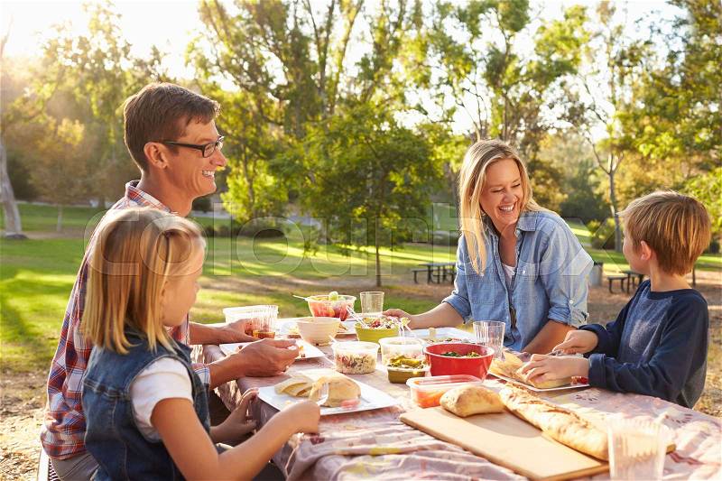Young white family enjoying a picnic at a table in a park, stock photo