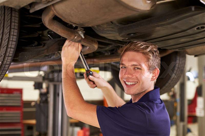 Portrait Of Auto Mechanic Working Underneath Car In Garage, stock photo