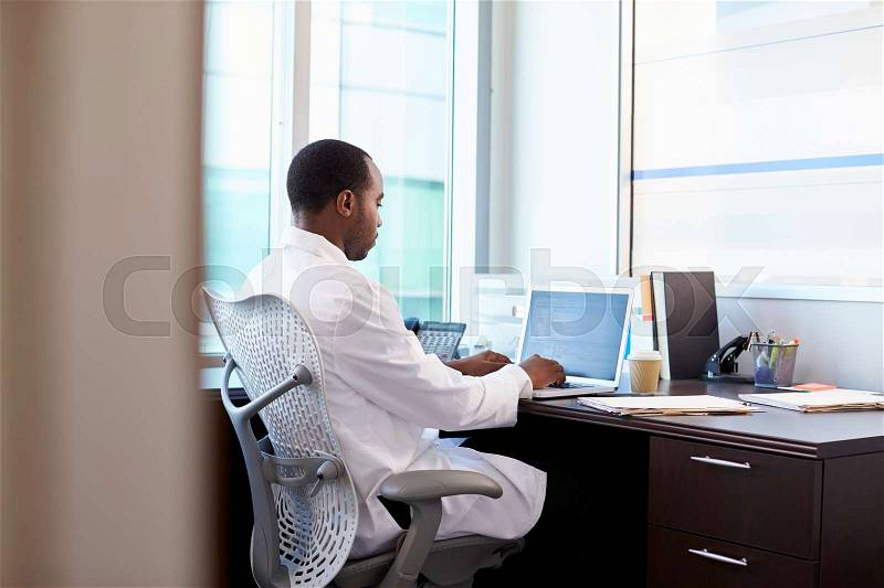 Doctor Wearing White Coat Working On Laptop In Office, stock photo