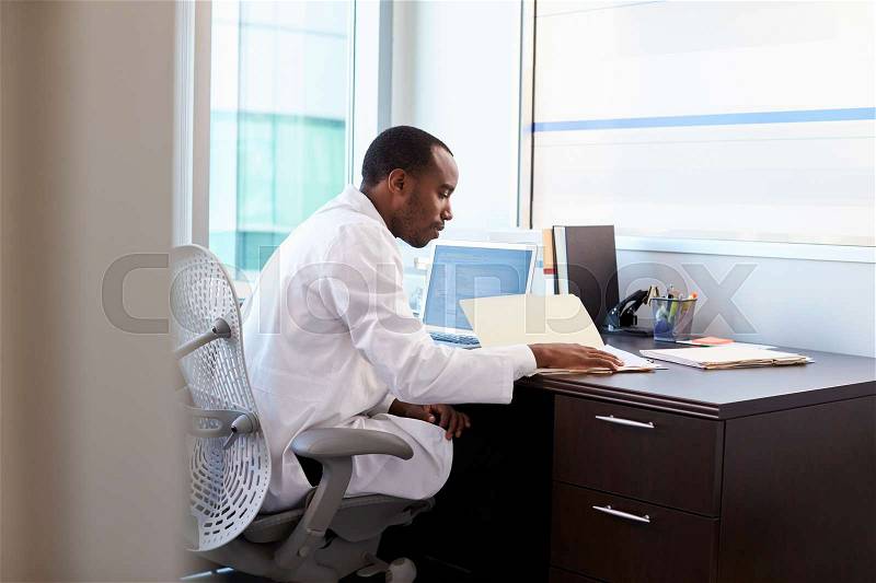 Doctor Wearing White Coat Reading Notes In Office, stock photo
