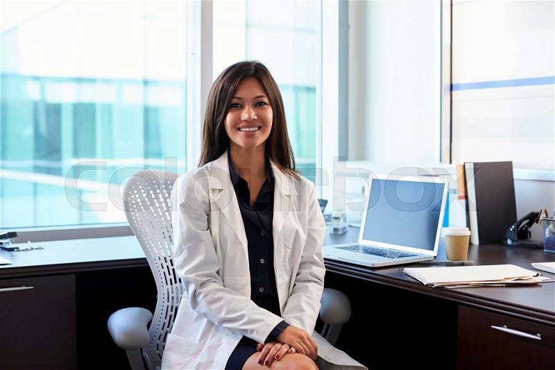 Portrait Of Female Doctor Wearing White Coat In Office, stock photo