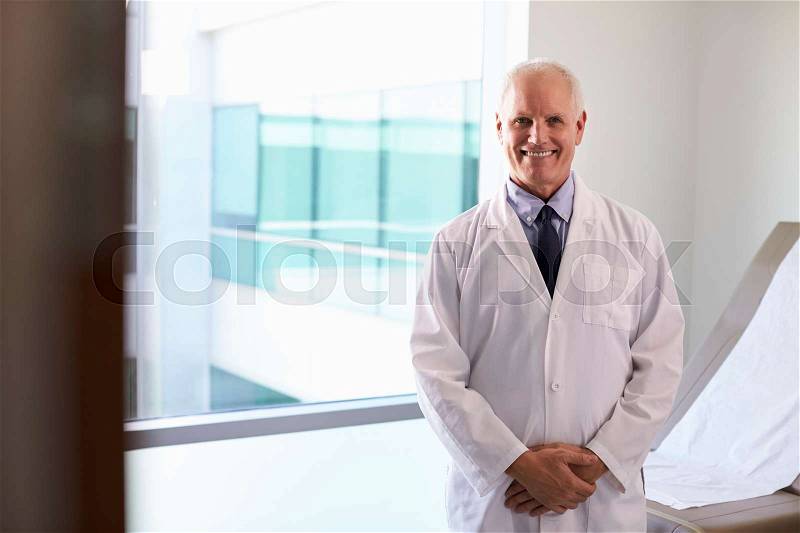 Portrait Of Male Doctor Wearing White Coat In Exam Room, stock photo