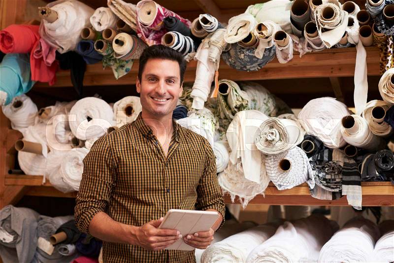 Man using tablet in fabric storage warehouse, portrait, stock photo