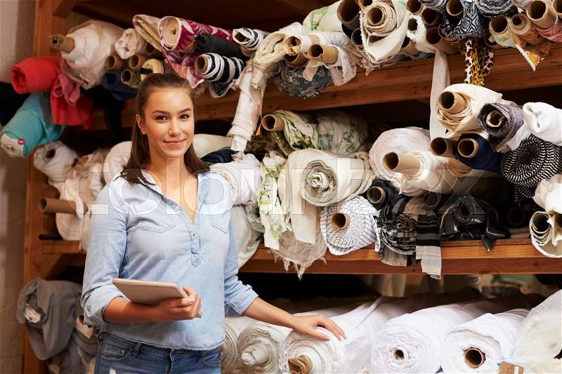 Woman using tablet in fabric storage warehouse, portrait, stock photo