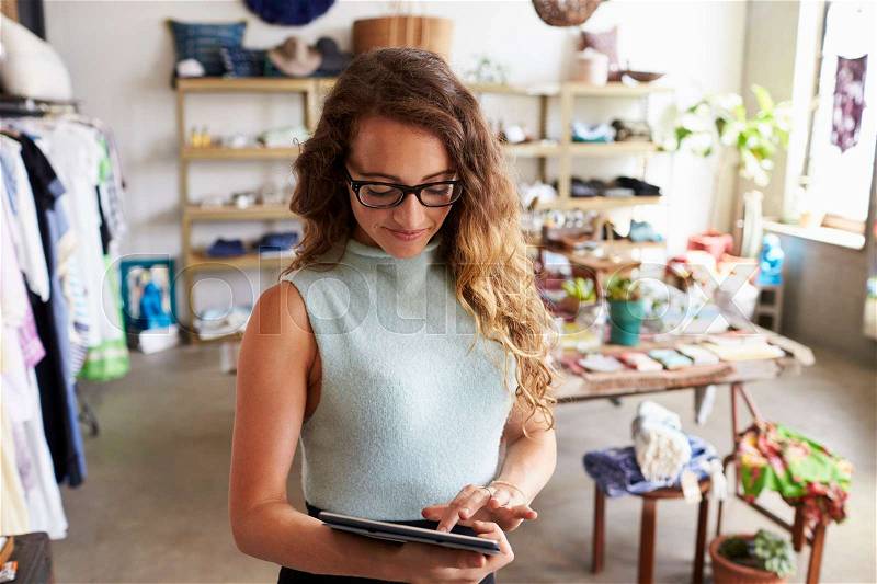 Female business owner using tablet computer in clothes shop, stock photo