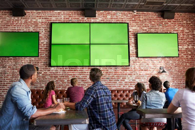 Rear View Of Friends Watching Game In Sports Bar On Screens, stock photo
