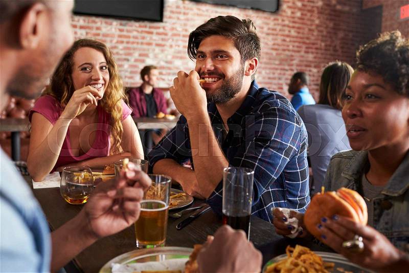 Friends Eating Out In Sports Bar With Screens In Background, stock photo