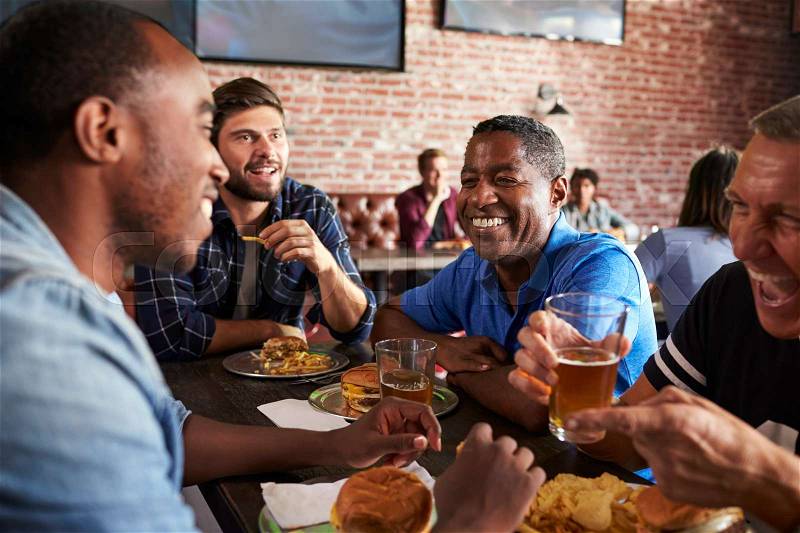 Male Friends Eating Out In Sports Bar With Screens In Behind, stock photo