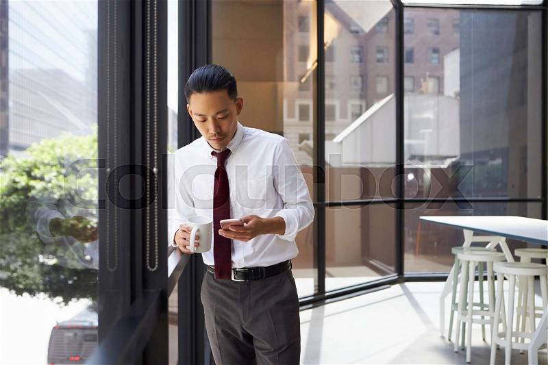 Asian businessman standing in modern office using phone, stock photo