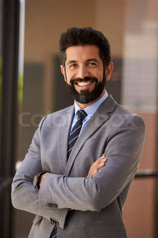 Smiling Hispanic businessman with arms crossed, vertical, stock photo