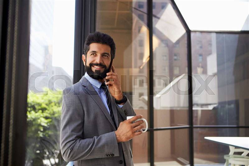 Middle aged Hispanic businessman using phone and holding cup, stock photo