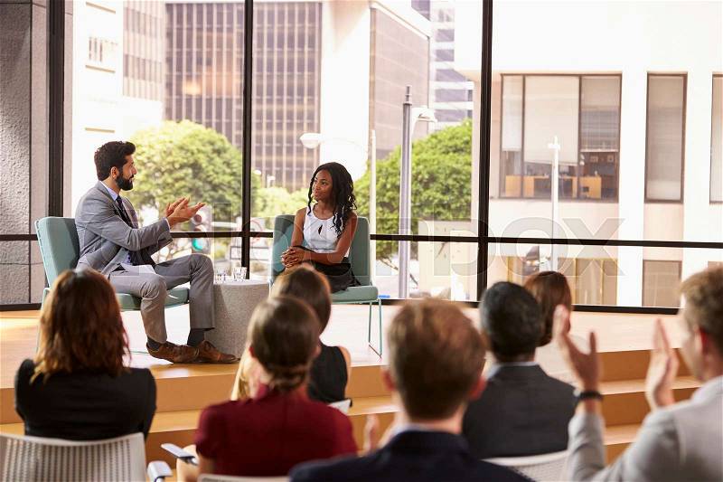 Man and woman talk in front of audience at business seminar, stock photo