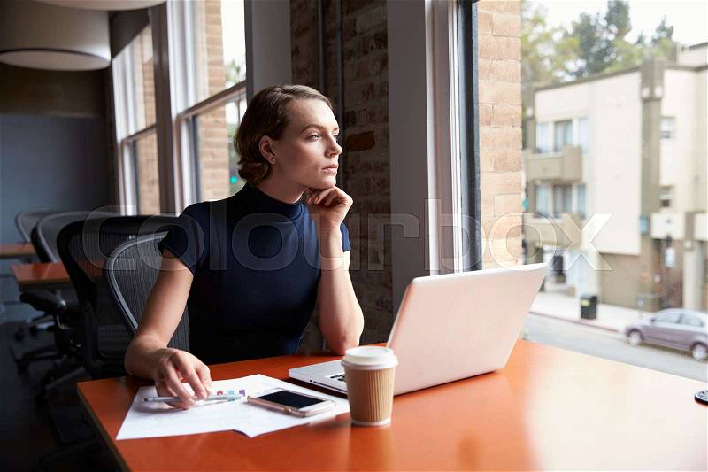 Thoughtful Businesswoman Working On Laptop By Window, stock photo