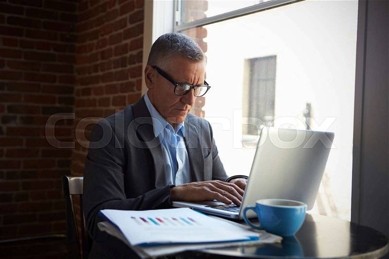 Mature Businessman Working On Laptop By Office Window, stock photo