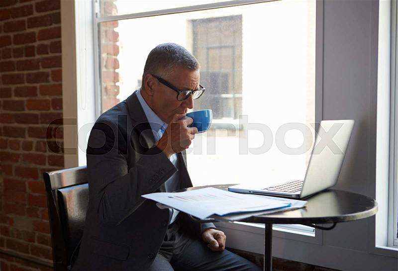 Mature Businessman Working On Laptop By Office Window, stock photo