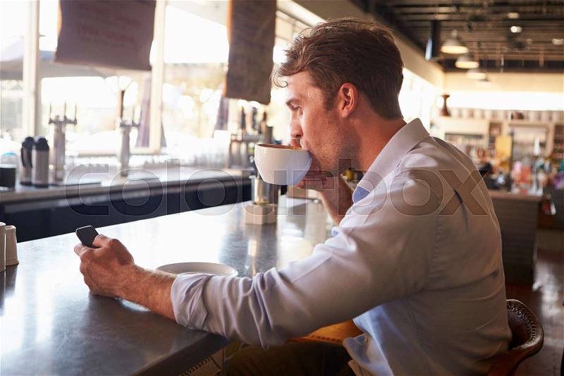 Man Checking Messages On Phone In Coffee Shop, stock photo