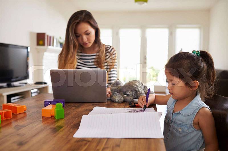 Mother Works On Laptop As Daughter Draws Picture In Book, stock photo