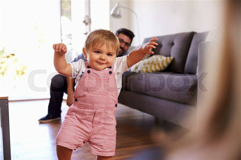 Parents Watching Baby Daughter Take First Steps At Home, stock photo
