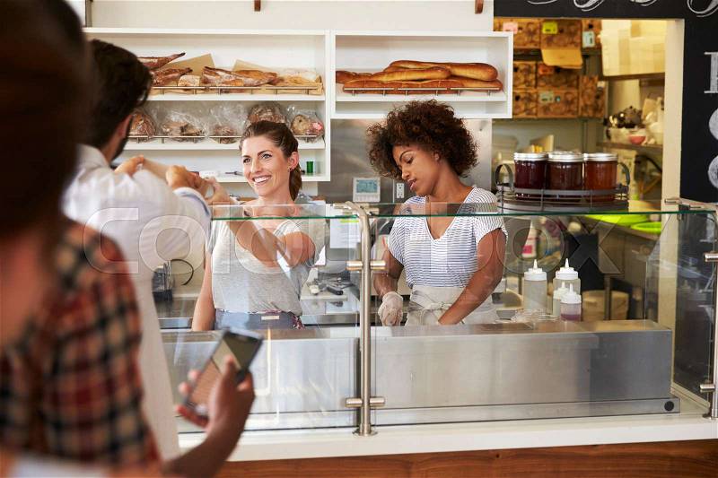 A queue of customers served by two women at a sandwich bar, stock photo