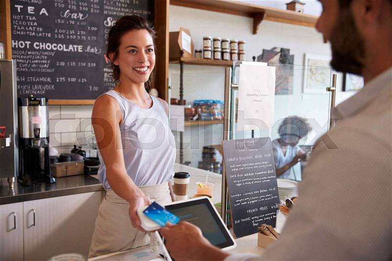 Customer at coffee shop pays smiling waitress with card, stock photo