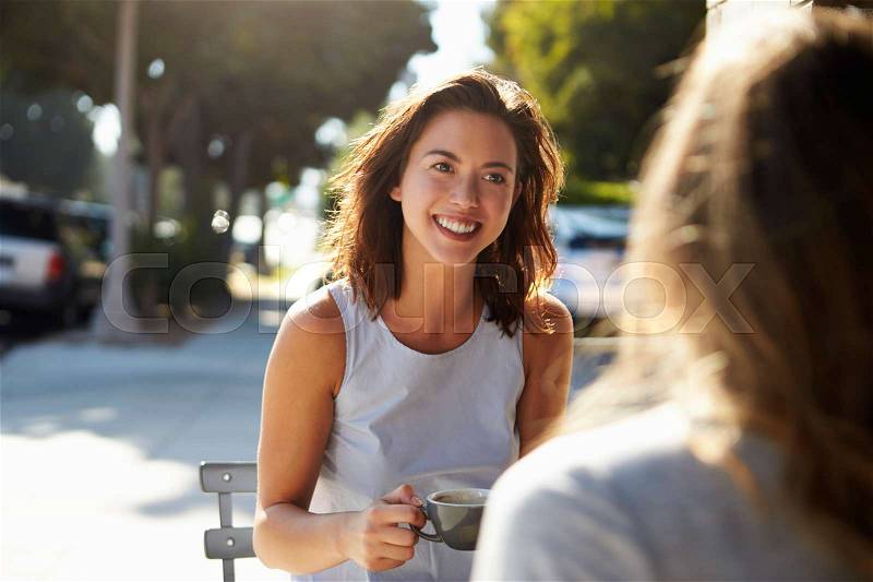 Two female friends talking over coffee outside a cafe, stock photo