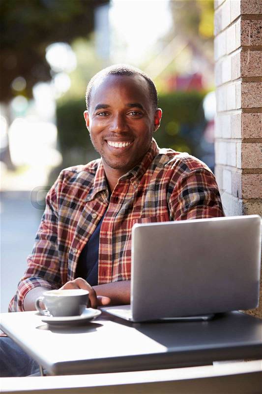 Young black man with laptop outside a cafe looking to camera, stock photo