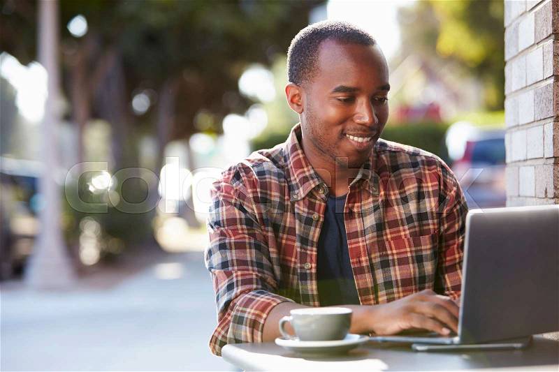 Young black man using a laptop computer outside a cafe, stock photo