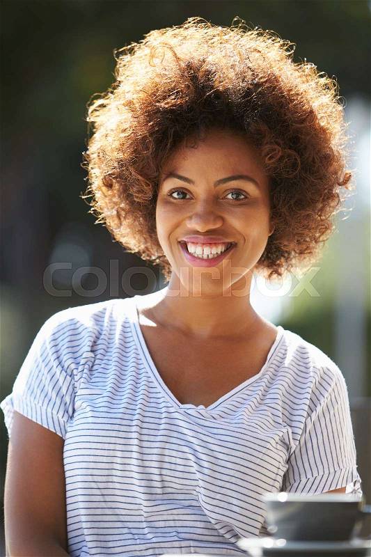 Happy young black woman sitting outside a cafe, vertical, stock photo