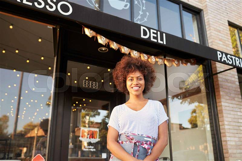 Black female business owner standing outside cafe shopfront, stock photo