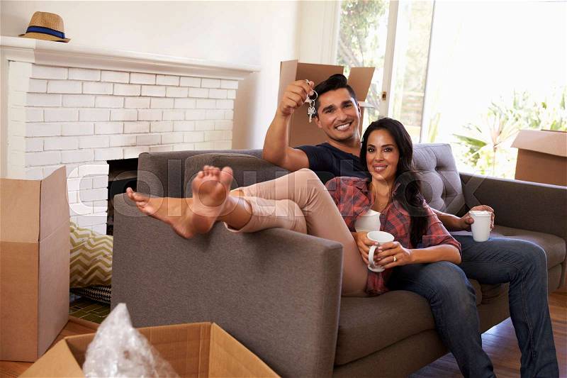Couple On Sofa Holding Keys Taking A Break On Moving Day, stock photo
