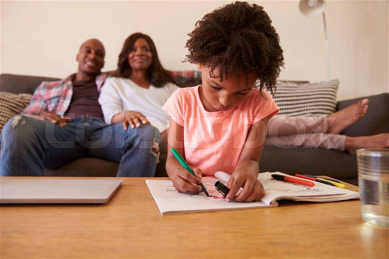 Parents Watch TV As Daughter Colors In Picture Book, stock photo